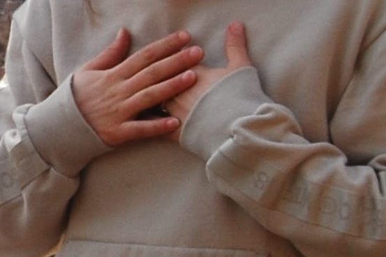Een vrouw met hoodie legt haar handen op de borst.