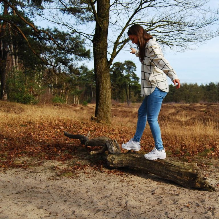 Persoon balanceert op een boomstam in de duinen van een bosrijk gebied.