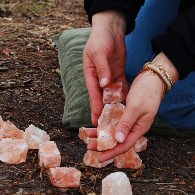 Handen die op de grond roze zoutkristallen plaatsen tijdens ervaringsgerichte therapie.